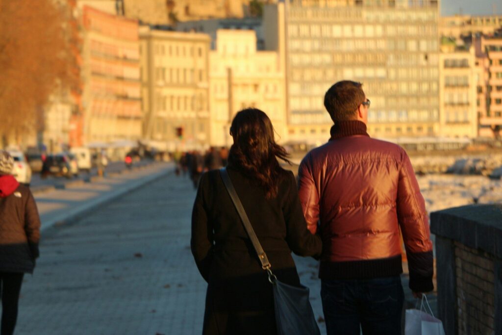Couple walking along a waterfront with buildings.